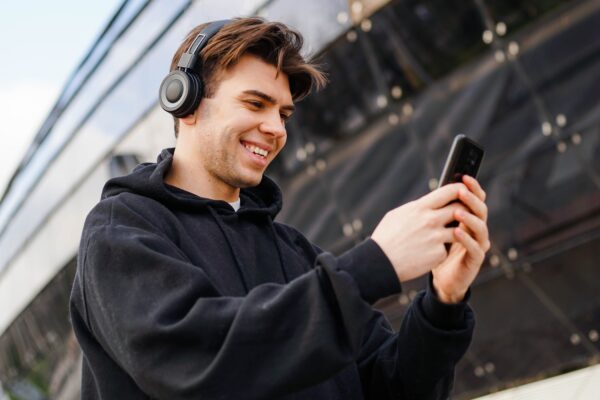 Young,Caucasian,Man,In,Headphones,Using,Smartphone,Texting,And,Listening